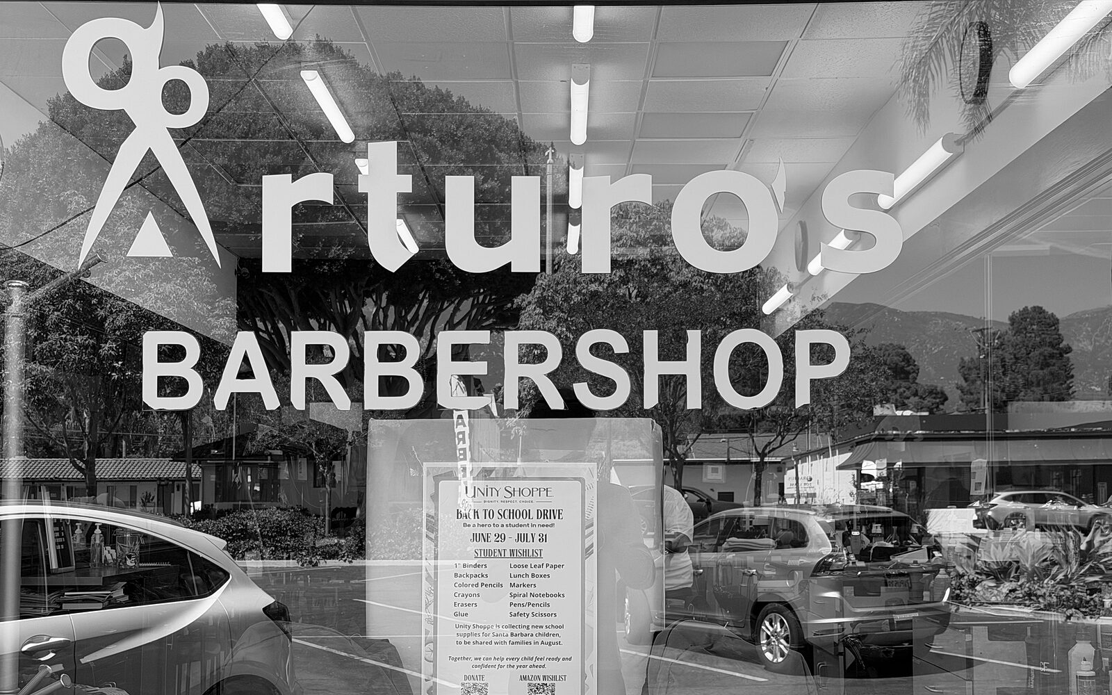 Arturo's Barbershop storefront window in Santa Barbara with a back-to-school supply drive poster